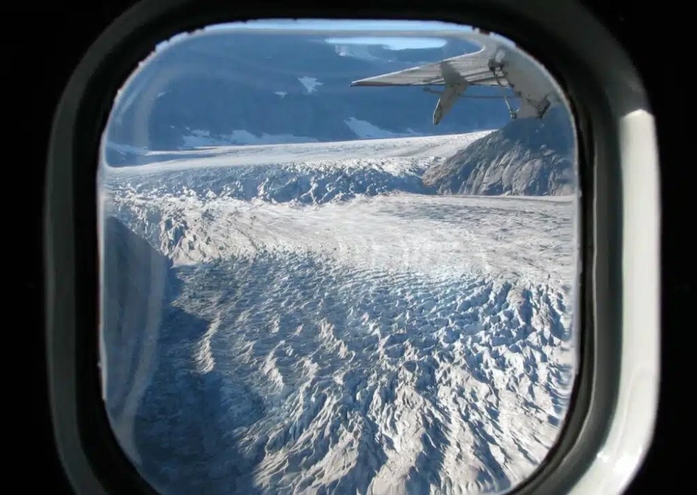 View from a Wings Airways window seat overlooking the Juneau Icefield and a de Havilland Otter flying above the glaciers in Southeast Alaska.